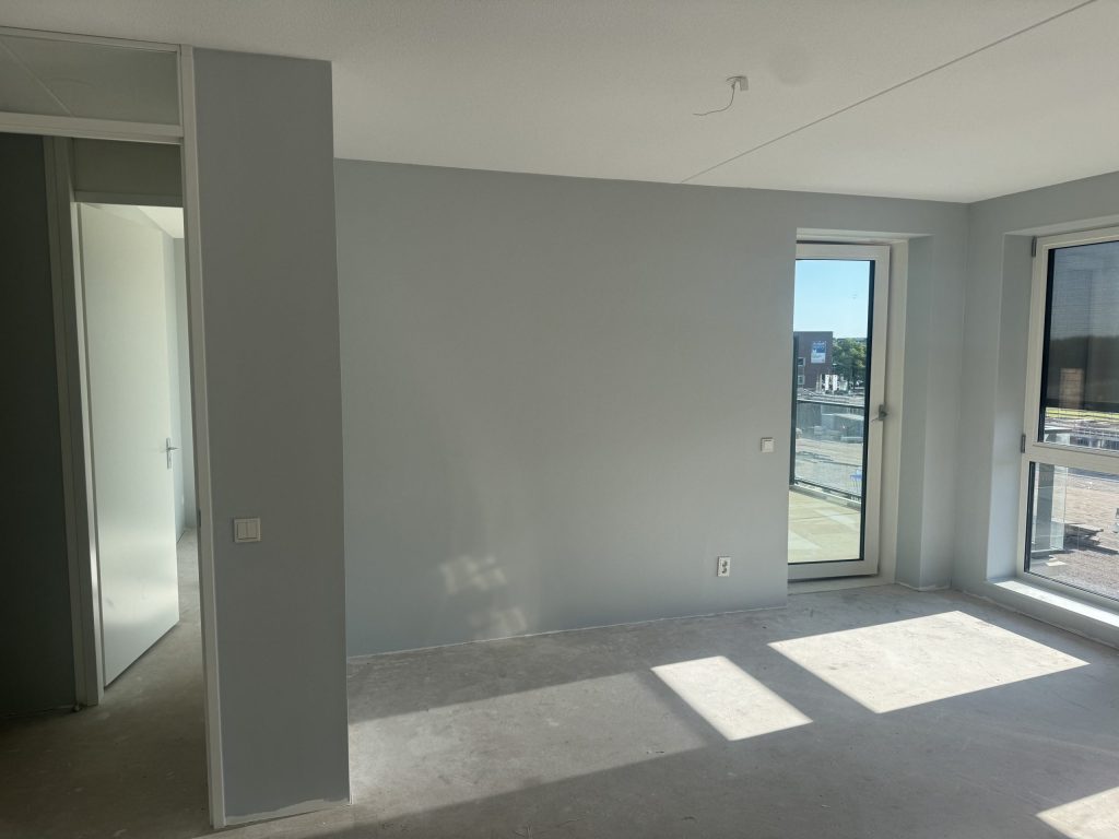 Appartement met lichtgrijs gesausde wanden, een balkondeur en grote ramen