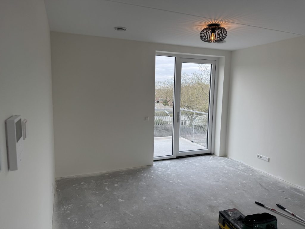 Lege kamer op een hogere verdieping met balkondeur en strakke witte wanden na het behangen
